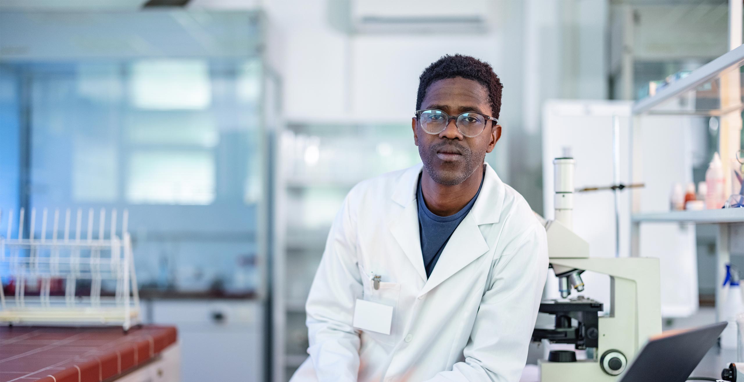 Medical researcher in a white lab coat, leaning against a laboratory counter.